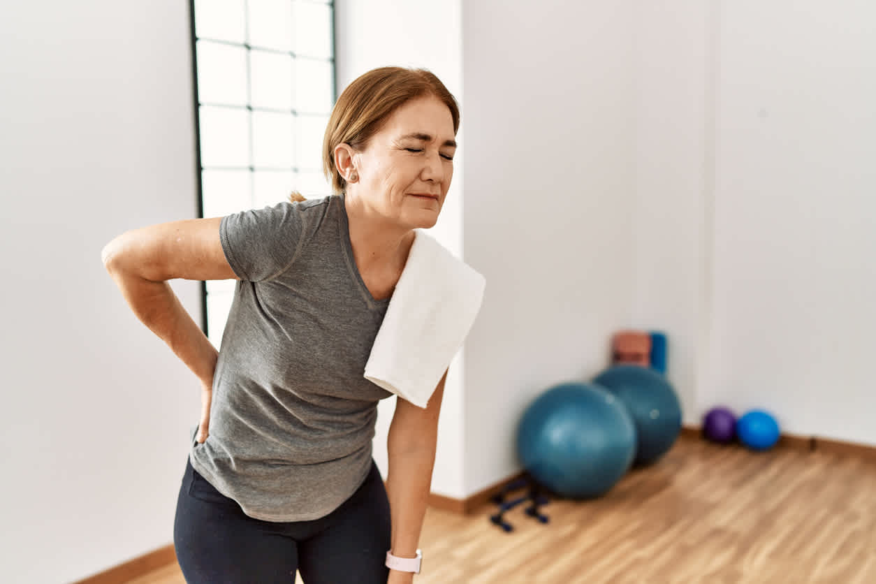Person in workout clothes experiencing DOMS and needing treatment with exercise equipment visible in background