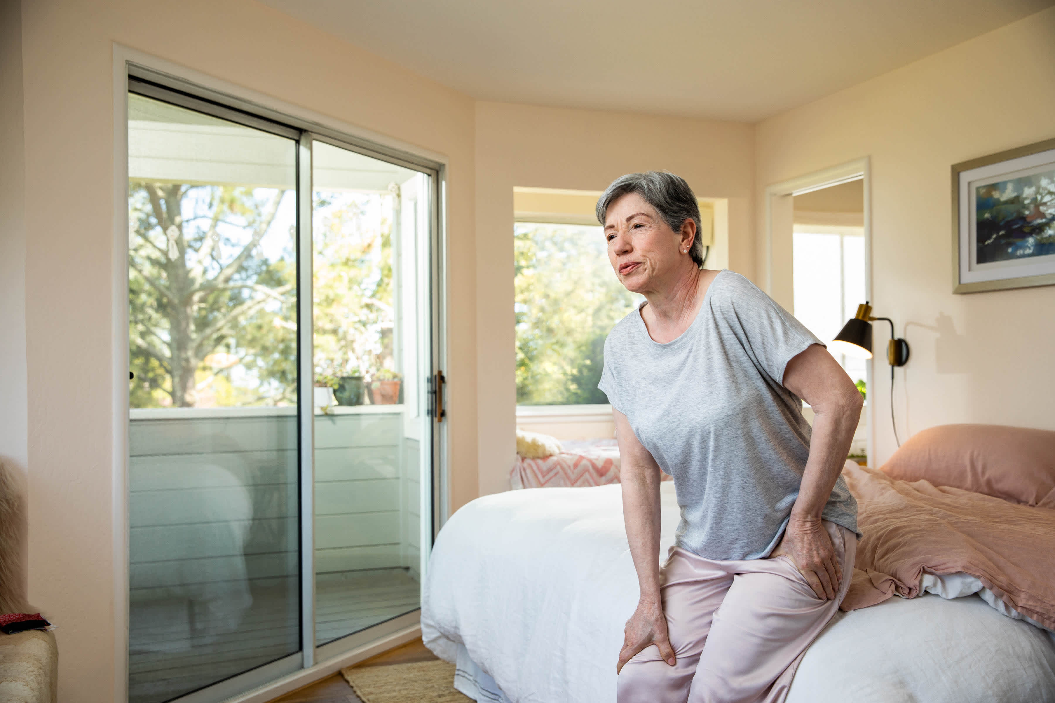 Elderly-woman-holding-her-hip-in-pain-while-getting-up-her-bed