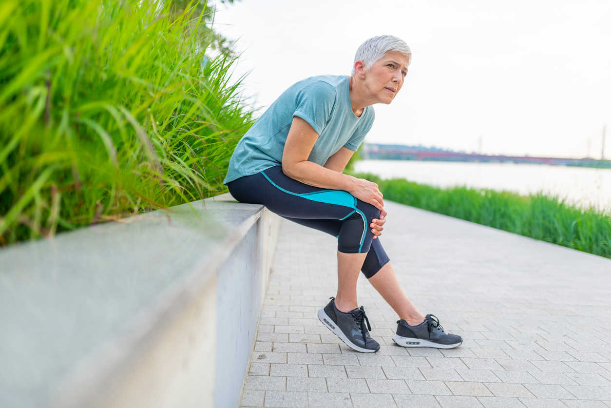 elderly-woman-touching-knee-in-pain-while-walking-outdoors