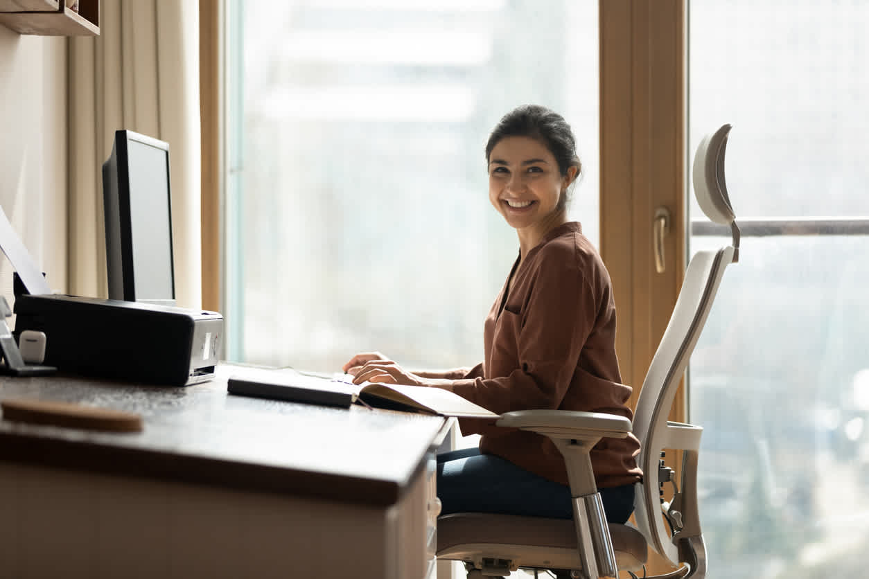 Image of a woman sitting at a desk in an office chair with light from a window shining into the room