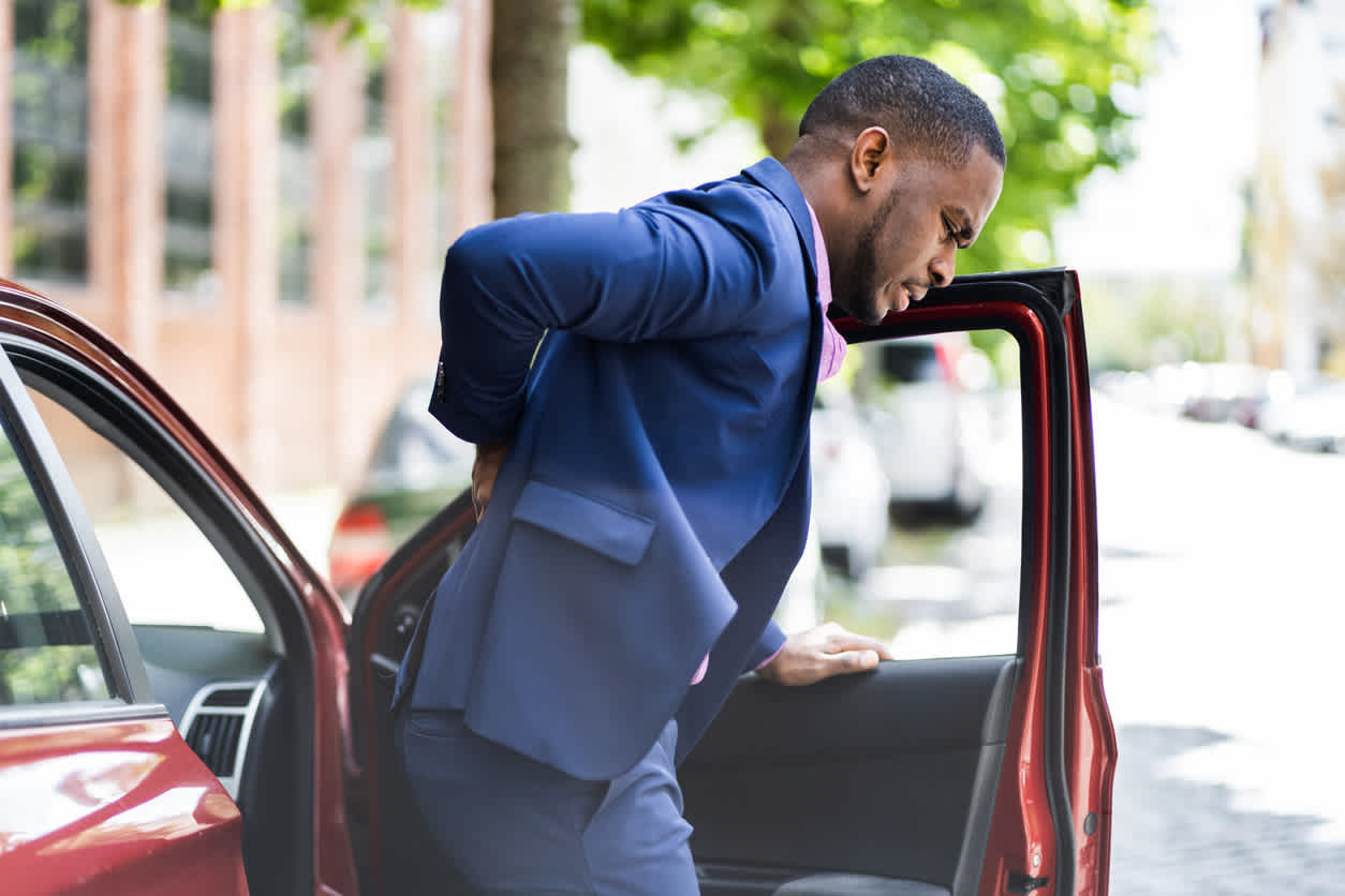 man-getting-off-a-car-holding-his-back-due-to-lumbar-strain
