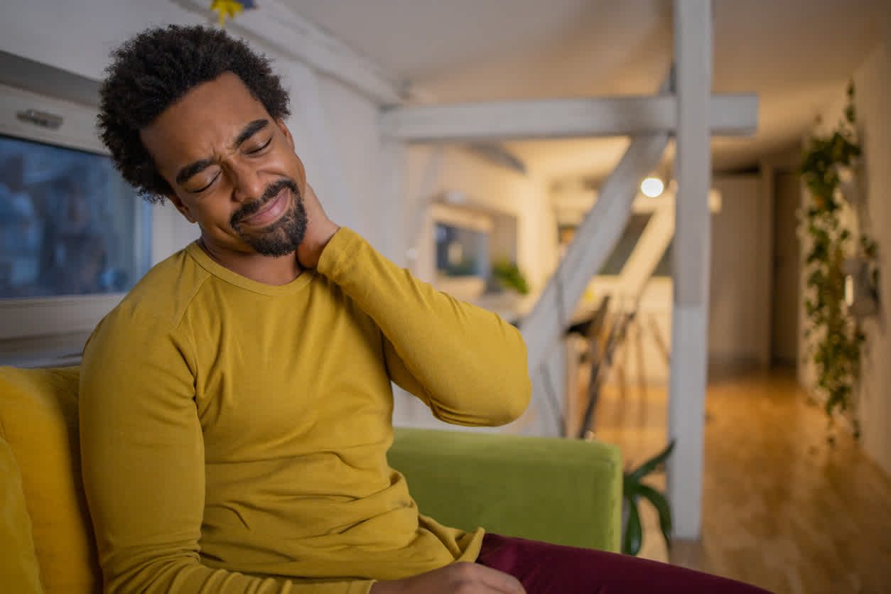 Man-holding-his-neck-in-pain-sitting-at-home
