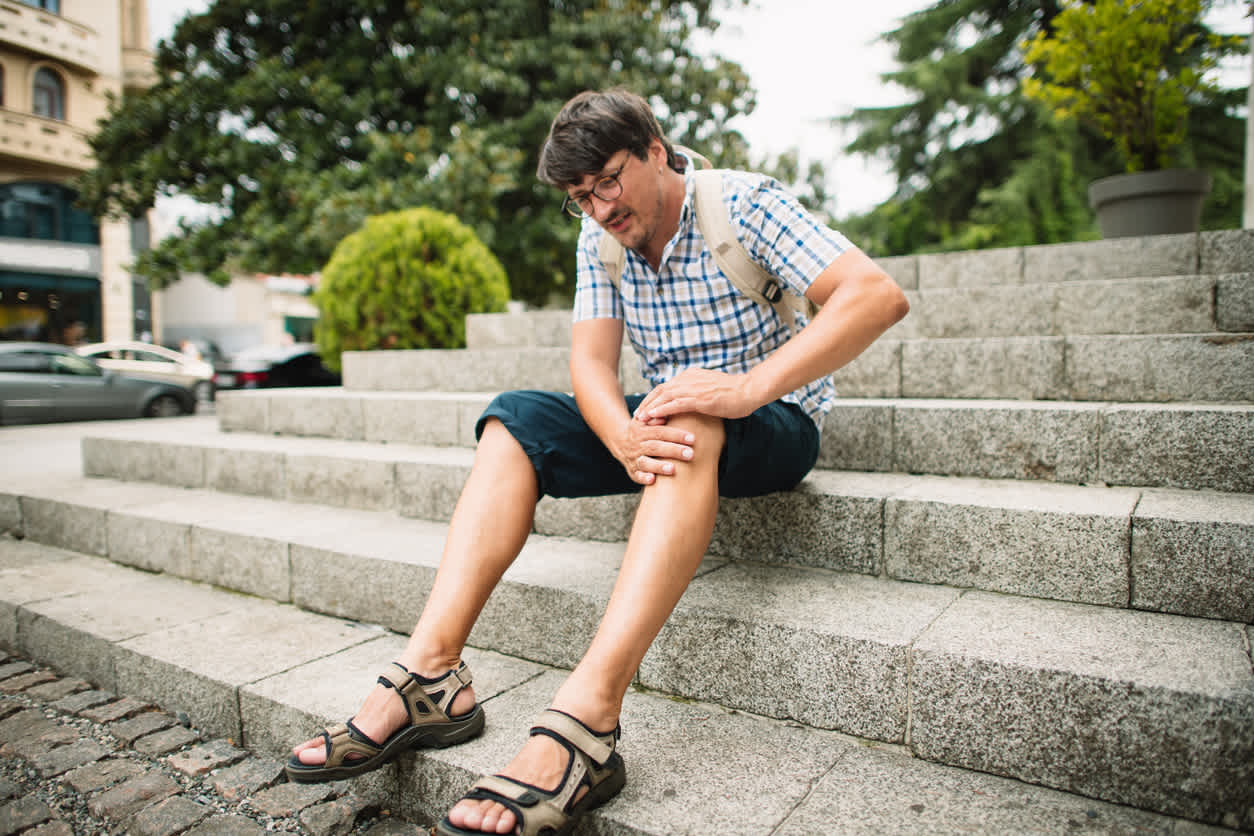 Man sitting down holding knee because of knee pain going down stairs.