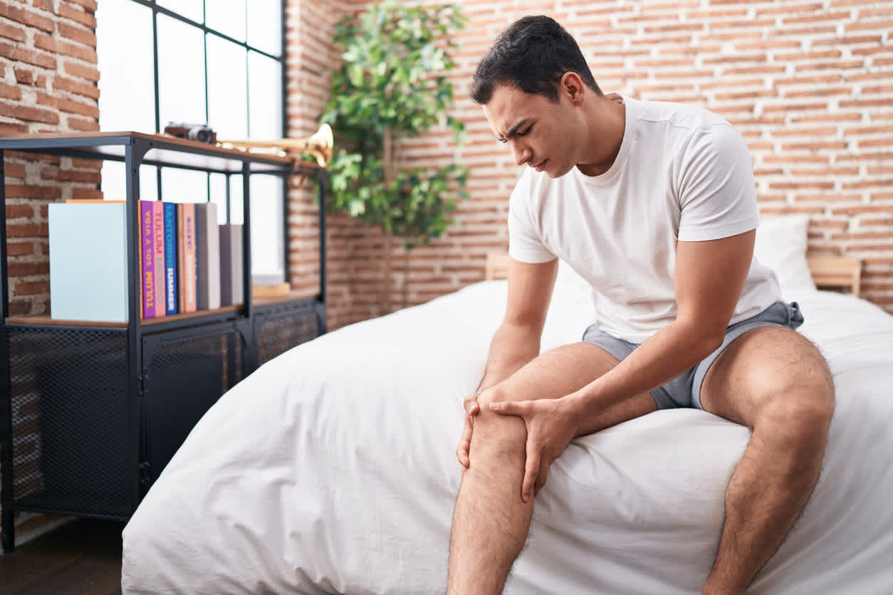 man-sitting-in-bed-touching-her-knee-worried