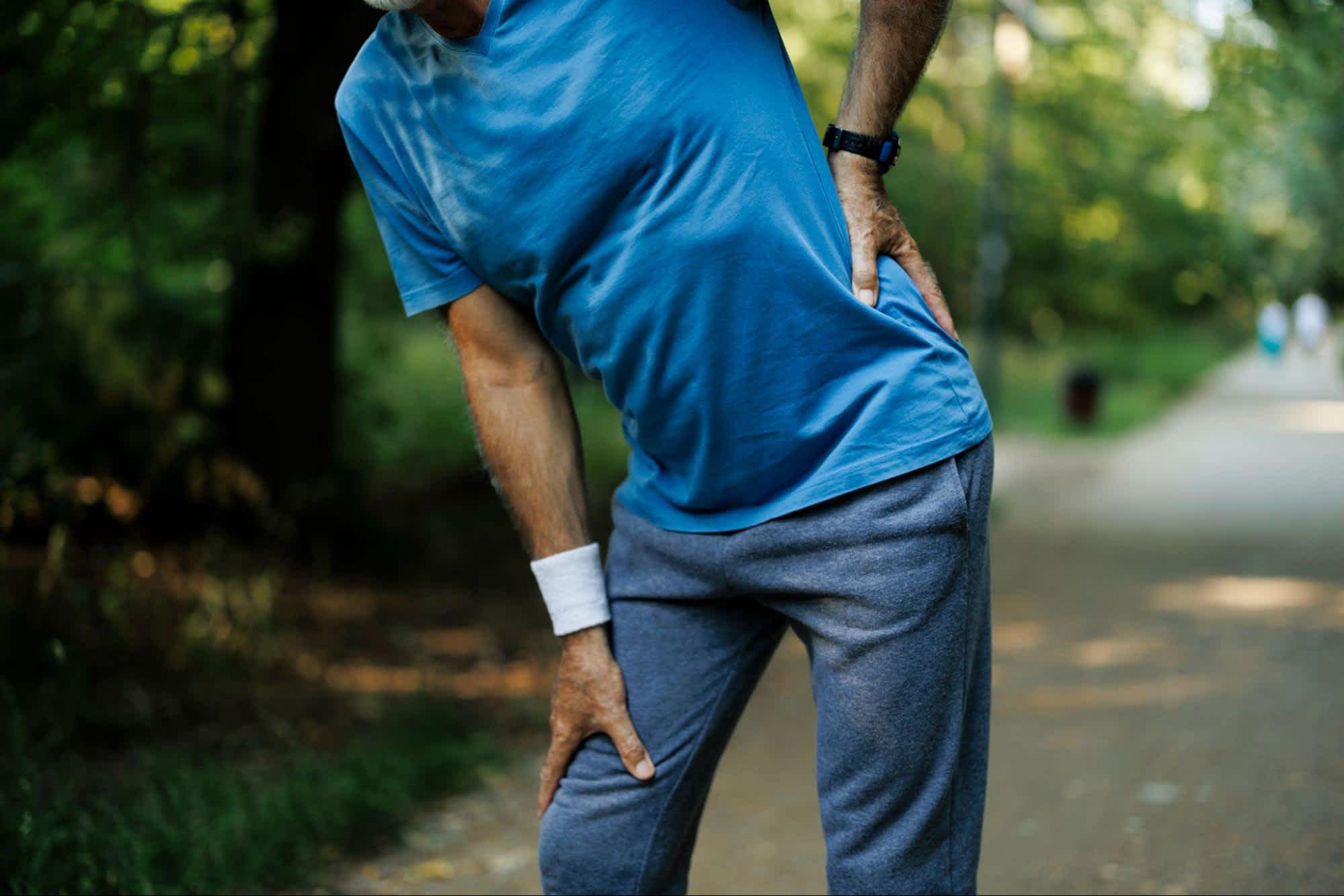 Person in blue shirt and sweatpants clutching their lower back in pain due to referred pain. 