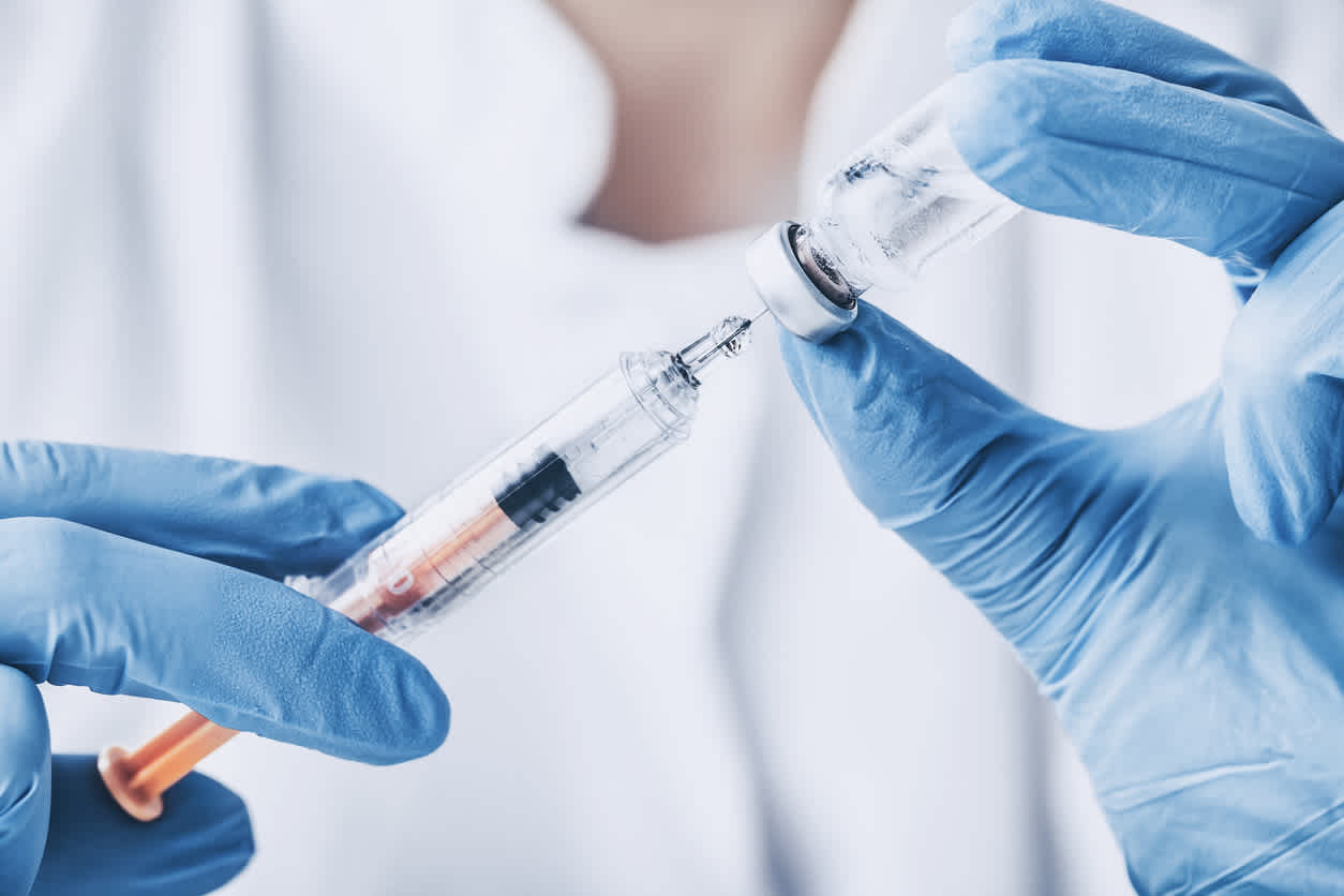 Gloved hands preparing steroid shots from vial against white background