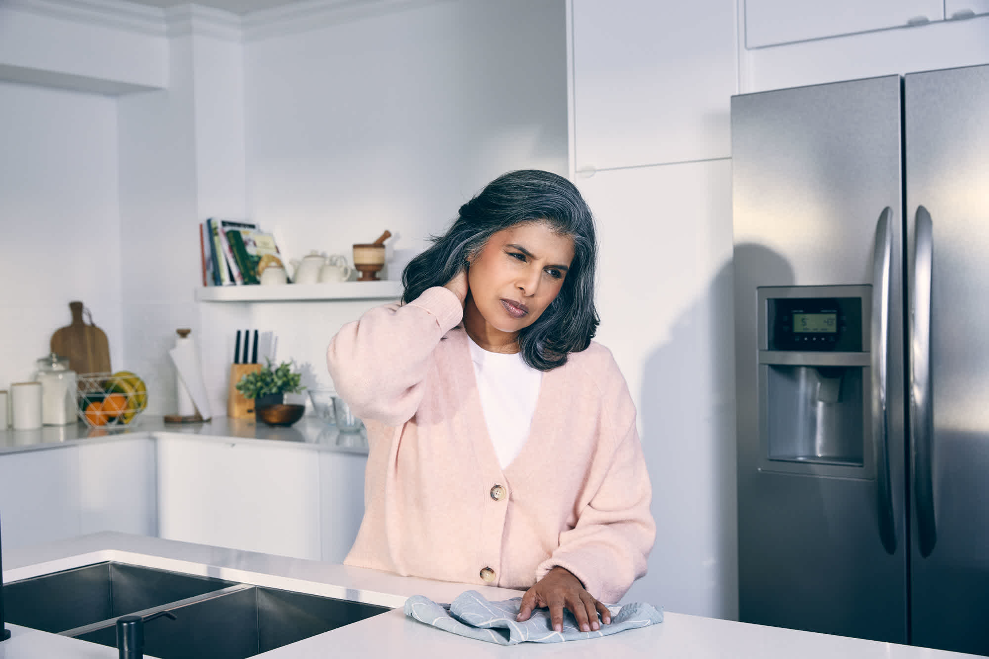 Woman-holding-her-neck-in-pain-at-her-kitchen