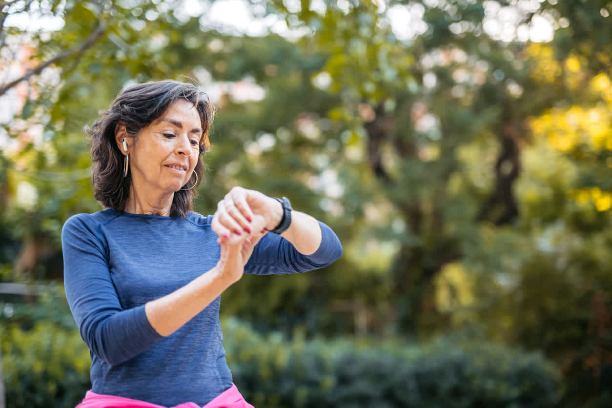 Active woman in blue long-sleeve shirt applying time management strategies and checking fitness tracker while exercising outdoors