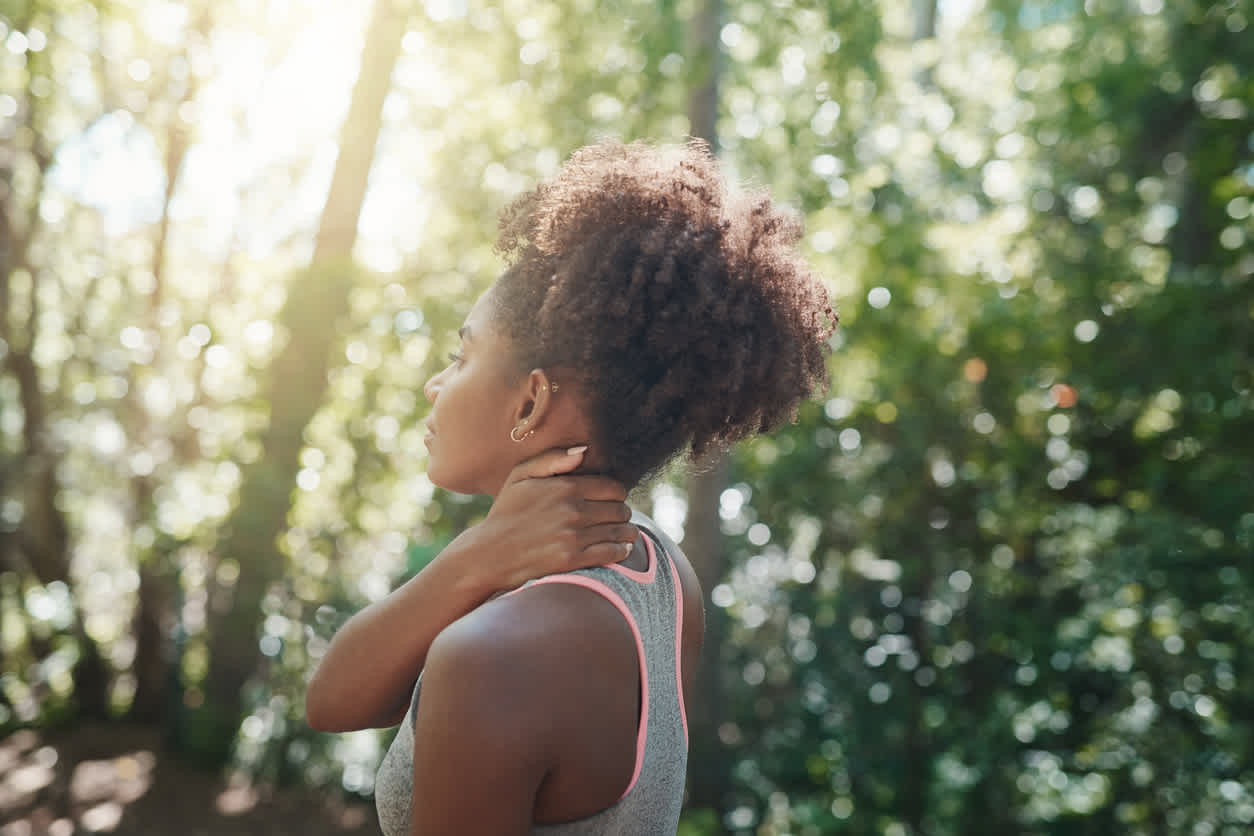 Person in athletic wear massaging neck while standing and wondering if she should work out with sore muscles.